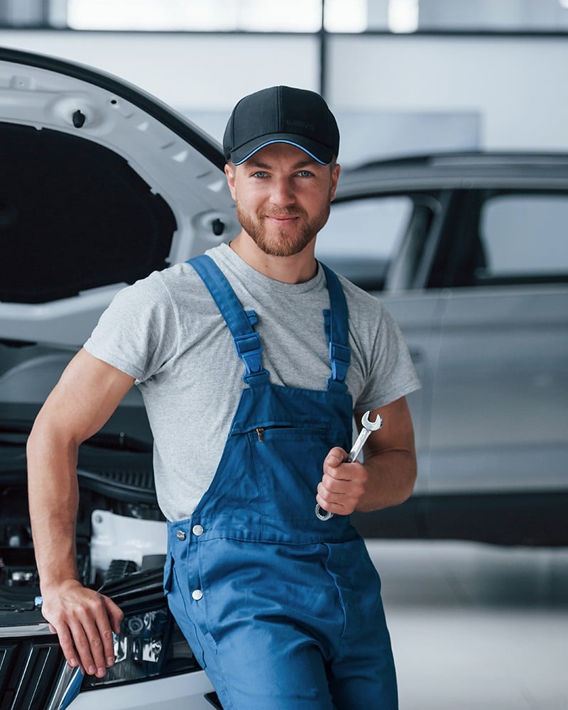 Mechanic holding wrench leaning on car.